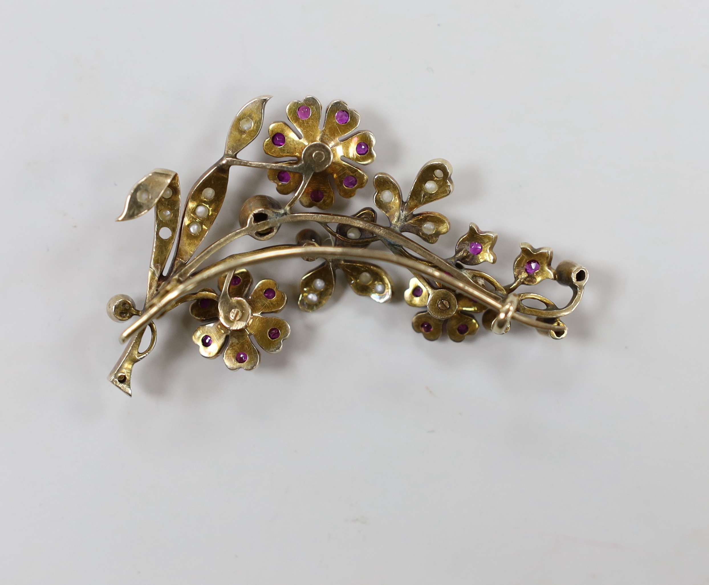 An early to mid 20th century, yellow metal, ruby and seed pearl cluster set floral spray brooch, 55mm, gross weight 13.3 grams (two pearls missing).